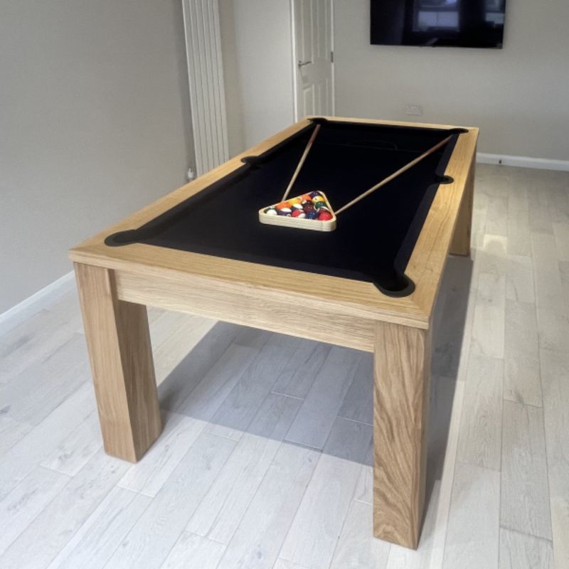Natural oak pool table with black felt top and pool balls in a modern room